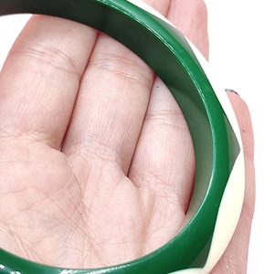May include: A circular bangle bracelet featuring a smooth, polished finish with a repeating geometric pattern of alternating deep forest green and creamy off-white curved segments that wrap around the entire circumference of the rigid band.