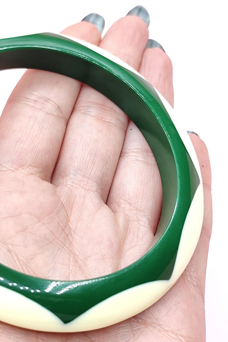 May include: A circular bangle bracelet featuring a smooth, polished finish with a repeating geometric pattern of alternating deep forest green and creamy off-white curved segments that wrap around the entire circumference of the rigid band.
