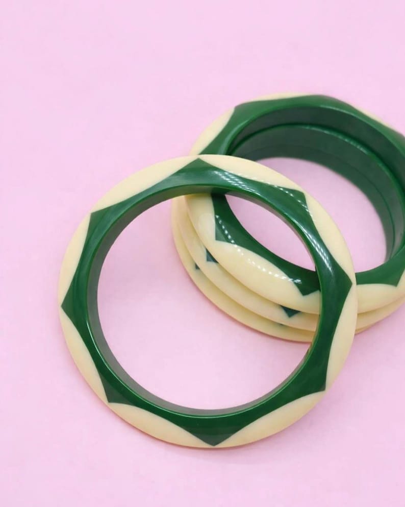 May include: A set of three circular bangle bracelets featuring a repeating geometric pattern of alternating cream and dark green segments. The bracelets have a smooth, polished finish and a consistent rounded profile, stacked partially overlapping each other.