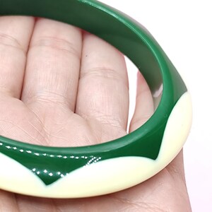 May include: A circular bangle bracelet featuring a smooth, glossy finish with a two-tone design. The bracelet alternates between deep forest green sections and creamy off-white, pointed petal-like shapes that wrap around the entire circumference.