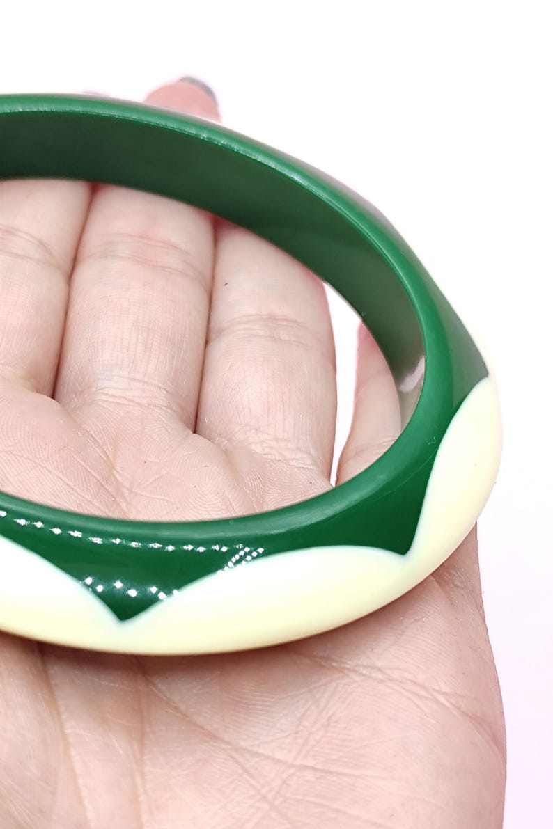May include: A circular bangle bracelet featuring a smooth, glossy finish with a two-tone design. The bracelet alternates between deep forest green sections and creamy off-white, pointed petal-like shapes that wrap around the entire circumference.