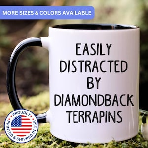 May include: A white ceramic mug with a black interior and handle. The text EASILY DISTRACTED BY DIAMONDBACK TERRAPINS is printed in black on the front. A circular badge with the American flag and the text PROUDLY PRINTED & SHIPPED IN USA is visible.