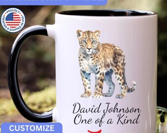 May include: A white ceramic mug with a black handle and interior, featuring a watercolor illustration of a leopard. Below the leopard, the text reads David Johnson One of a Kind in a black script font. The mug includes a circular US flag emblem.