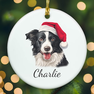May include: A round white ceramic ornament featuring a black and white Border Collie dog wearing a red and white Santa hat. The dog has its mouth open with its tongue visible. The name Charlie is printed in black cursive script below the dog.