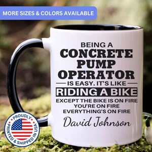 May include: A white ceramic mug with a black interior and handle, featuring black text that reads: BEING A CONCRETE PUMP OPERATOR IS EASY. IT'S LIKE RIDING A BIKE EXCEPT THE BIKE IS ON FIRE YOU'RE ON FIRE EVERYTHING'S ON FIRE David Johnson.