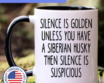 May include: A white ceramic mug with a black handle and interior, featuring the black text: SILENCE IS GOLDEN UNLESS YOU HAVE A SIBERIAN HUSKY THEN SILENCE IS SUSPICIOUS. A circular badge with the American flag and text is visible on the lower left.