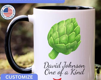 May include: A white ceramic mug with a black handle and interior, featuring a green artichoke illustration and the black text David Johnson One of a Kind printed on the front. The mug has a smooth finish and a standard cylindrical shape.