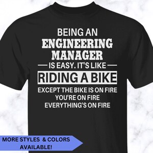 May include: A black short-sleeved t-shirt featuring white text that reads: BEING AN ENGINEERING MANAGER IS EASY. IT'S LIKE RIDING A BIKE EXCEPT THE BIKE IS ON FIRE YOU'RE ON FIRE EVERYTHING'S ON FIRE. The shirt has a crew neckline and a standard fit.