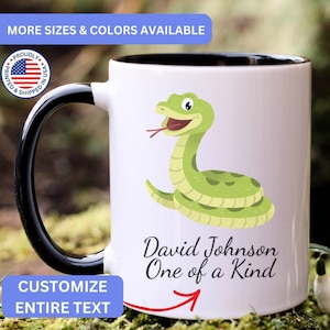 May include: A white ceramic mug with a black handle and interior, featuring a cartoon green snake illustration and the text David Johnson One of a Kind. The mug includes a circular badge with a US flag and the text PROUDLY SHIPPED IN USA.