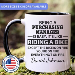 May include: A white ceramic mug with a black interior and handle, featuring black text that reads: BEING A PURCHASING MANAGER IS EASY. IT'S LIKE RIDING A BIKE EXCEPT THE BIKE IS ON FIRE YOU'RE ON FIRE EVERYTHING'S ON FIRE David Johnson.