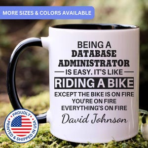 May include: White ceramic mug with a black handle and interior. The mug features the text: "BEING A DATABASE ADMINISTRATOR IS EASY. IT'S LIKE RIDING A BIKE EXCEPT THE BIKE IS ON FIRE YOU'RE ON FIRE EVERYTHING'S ON FIRE David Johnson."