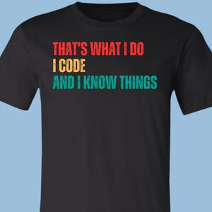 May include: A black short-sleeved t-shirt featuring the text THAT'S WHAT I DO in red, I CODE in yellow, and AND I KNOW THINGS in teal. The graphic is centered on the chest and uses a distressed, retro-inspired font style on the cotton fabric.