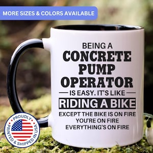 May include: A white ceramic mug with a black handle and interior, featuring black text that reads: BEING A CONCRETE PUMP OPERATOR IS EASY. IT'S LIKE RIDING A BIKE EXCEPT THE BIKE IS ON FIRE YOU'RE ON FIRE EVERYTHING'S ON FIRE. Includes a US flag emblem.