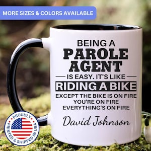 May include: White ceramic mug with a black handle and interior. The mug features the text "BEING A PAROLE AGENT IS EASY. IT'S LIKE RIDING A BIKE EXCEPT THE BIKE IS ON FIRE YOU'RE ON FIRE EVERYTHING'S ON FIRE" and the name "David Johnson".