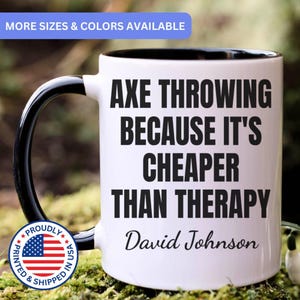 May include: A white ceramic mug with a black interior and handle. The mug features the black text "AXE THROWING BECAUSE IT'S CHEAPER THAN THERAPY" and the name "David Johnson" printed on the front. A circular badge with the US flag is visible.