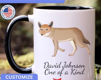May include: A white ceramic mug with a black handle and interior. The mug features a tan coyote illustration and the black text "David Johnson One of a Kind" printed on the front. The design includes a red arrow pointing toward the text.