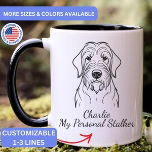 May include: A white ceramic mug with a black interior and handle, featuring a black line art illustration of a dog's face. Below the dog, the text reads Charlie My Personal Stalker in a black script font, with a red arrow pointing toward the text.