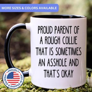 May include: A white ceramic mug with a black interior and a black handle. The mug features black text that reads: PROUD PARENT OF A ROUGH COLLIE THAT IS SOMETIMES AN ASSHOLE AND THAT'S OKAY. A circular badge with the American flag is visible.