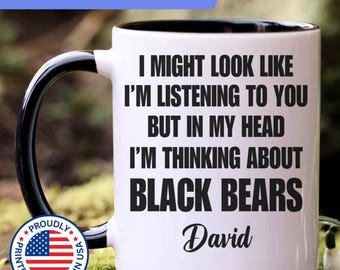 May include: A white ceramic mug with a black interior and handle, featuring the black text: I MIGHT LOOK LIKE I'M LISTENING TO YOU BUT IN MY HEAD I'M THINKING ABOUT BLACK BEARS, followed by the name David in a cursive script font.
