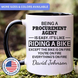 May include: A white ceramic mug with a black interior and handle. The front features black text that reads: BEING A PROCUREMENT AGENT IS EASY. IT'S LIKE RIDING A BIKE EXCEPT THE BIKE IS ON FIRE YOU'RE ON FIRE EVERYTHING'S ON FIRE David Johnson.