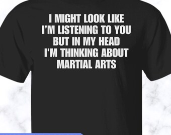 May include: A black short-sleeved t-shirt featuring white text that reads: I MIGHT LOOK LIKE I'M LISTENING TO YOU BUT IN MY HEAD I'M THINKING ABOUT MARTIAL ARTS. The shirt has a crew neckline and a standard fit, displaying the printed message clearly.