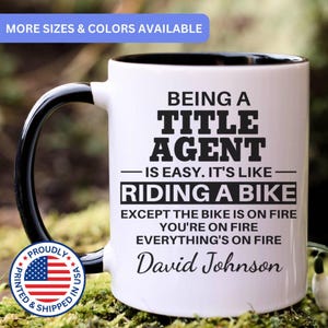 May include: A white ceramic mug with a black handle and interior. The mug features the text "BEING A TITLE AGENT IS EASY. IT'S LIKE RIDING A BIKE EXCEPT THE BIKE IS ON FIRE YOU'RE ON FIRE EVERYTHING'S ON FIRE David Johnson."