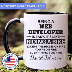 May include: A white ceramic mug with a black interior and handle, featuring black text that reads: BEING A WEB DEVELOPER IS EASY. IT'S LIKE RIDING A BIKE EXCEPT THE BIKE IS ON FIRE YOU'RE ON FIRE EVERYTHING'S ON FIRE David Johnson.