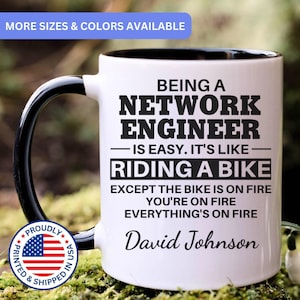 May include: White ceramic mug with a black handle and interior. The mug features the text "BEING A NETWORK ENGINEER IS EASY. IT'S LIKE RIDING A BIKE EXCEPT THE BIKE IS ON FIRE YOU'RE ON FIRE EVERYTHING'S ON FIRE" and the name "David Johnson".