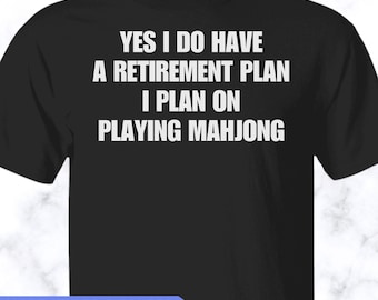 May include: A black short-sleeved t-shirt featuring white text that reads: YES I DO HAVE A RETIREMENT PLAN I PLAN ON PLAYING MAHJONG. The shirt has a crew neckline and a standard fit, with a blue banner at the bottom stating MORE STYLES & COLORS AVAILABLE!
