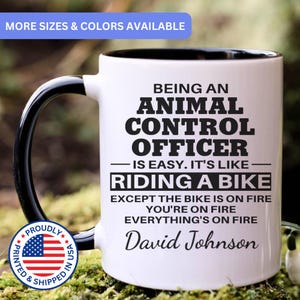 May include: White ceramic mug with a black handle and interior rim. The mug features the text "BEING AN ANIMAL CONTROL OFFICER IS EASY. IT'S LIKE RIDING A BIKE EXCEPT THE BIKE IS ON FIRE YOU'RE ON FIRE EVERYTHING'S ON FIRE David Johnson."