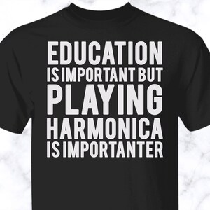 May include: A black short-sleeved t-shirt featuring white text that reads: EDUCATION IS IMPORTANT BUT PLAYING HARMONICA IS IMPORTANTER. The shirt has a crew neckline and is made of a solid black fabric with bold, capitalized white lettering centered on the front.