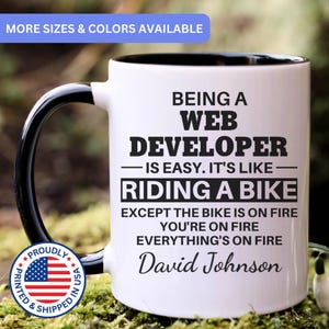 May include: White ceramic mug with a black handle and rim. The mug features the text "BEING A WEB DEVELOPER - IS EASY. IT'S LIKE - RIDING A BIKE EXCEPT THE BIKE IS ON FIRE YOU'RE ON FIRE EVERYTHING'S ON FIRE David Johnson".