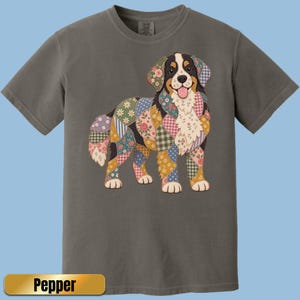 May include: A charcoal gray short-sleeve t-shirt featuring a graphic of a dog composed of various colorful floral and checkered quilt-style patches. The dog has a white chest, black ears, and a pink tongue. The text Pepper is visible below.