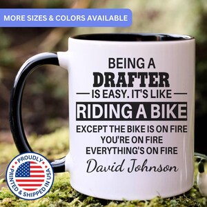 May include: White ceramic mug with a black handle and interior rim. The mug features the text "BEING A DRAFTER - IS EASY. IT'S LIKE - RIDING A BIKE EXCEPT THE BIKE IS ON FIRE YOU'RE ON FIRE EVERYTHING'S ON FIRE David Johnson".