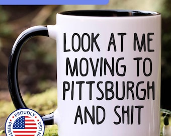 May include: A white ceramic mug with a black handle and interior, featuring the black printed text: LOOK AT ME MOVING TO PITTSBURGH AND SHIT. The mug includes a circular badge with the American flag and the text PROUDLY PRINTED & SHIPPED IN USA.