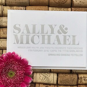 May include: A white wedding invitation card with gray text. The card reads "Sally & Michael" in large, bold letters. The text below reads "Would love you to join them to celebrate their wedding 17th February 2018, 1.30pm, The Tythe Barn, Anyho Drinks and Dancing to Follow."