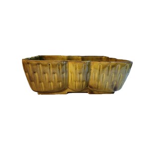 May include: A green ceramic planter with a unique, textured design. The planter has a rectangular shape with three rounded sections.