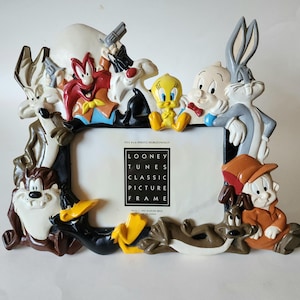 May include: A Looney Tunes picture frame featuring molded figures of Wile E. Coyote, Yosemite Sam, Sylvester, Tweety, Porky Pig, Bugs Bunny, Taz, Daffy Duck, and Elmer Fudd. The center insert reads: Fits 4x6 photo horizontally Looney Tunes Classic Picture Frame.
