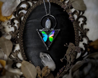 May include: A silver necklace with a iridescent butterfly charm set in a triangle pendant. The pendant is surrounded by a silver circle with a moonstone in the center.