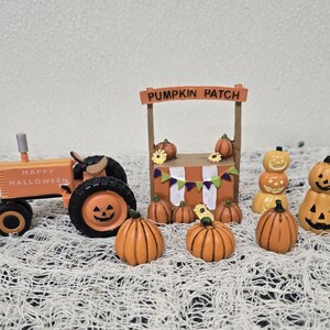 May include: Orange and black Halloween-themed miniature figurines. Includes a tractor with "Happy Halloween" text, a "Pumpkin Patch" stand, and various pumpkin figures. The scene is set on a white, textured surface.