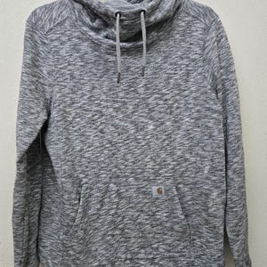 May include: A gray hooded sweatshirt with a cowl neck and a kangaroo pocket. The sweatshirt has a drawstring and a small logo patch on the pocket. The fabric has a heathered appearance.
