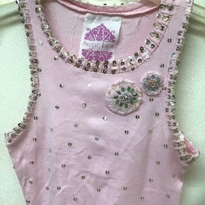 May include: A pink sleeveless tank top with a sequined trim and embellishments. The tank top has a small label that says "Sugar Lips".