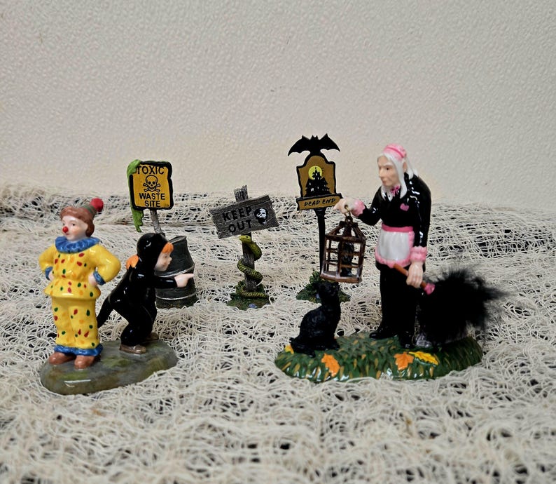 Peut inclure: Un ensemble de figurines miniatures d'Halloween comprenant un clown jaune, un personnage v&ecirc;tu de noir, un panneau de d&eacute;chets toxiques, un panneau keep out avec un serpent, un panneau dead end avec une chauve-souris et une figurine en noir et rose.