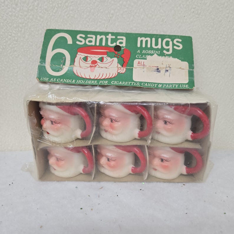 May include: A package of six Santa mugs. Each mug is white with a red handle and Santa's face. The package has a green label that reads "6 santa mugs" and "USE AS CANDLE HOLDERS, FOR CIGARETTES, CANDY & PARTY USE."