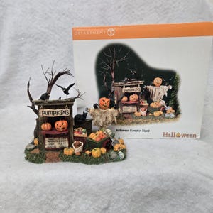 Peut inclure: Un ensemble de figurines miniatures Department 56 Halloween Pumpkin Stand comprenant un stand en bois avec une enseigne PUMPKINS, un &eacute;pouvantail, des corbeaux noirs, un chat noir et diverses citrouilles orange, avec sa bo&icirc;te en carton d'origine.