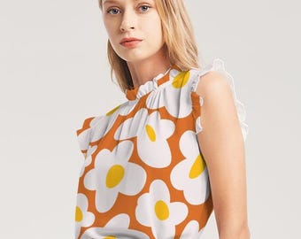 May include: A sleeveless blouse with a high neck and a ruffled collar. The blouse is orange with a white daisy print and yellow centers. The model is wearing a brown skirt.