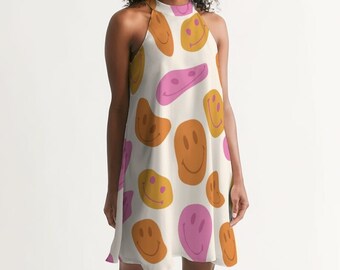 May include: A sleeveless, cream-colored dress featuring a repeating pattern of smiley faces in shades of orange, yellow, and pink. The dress has a halter neckline and a relaxed fit, suitable for casual wear.
