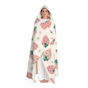 May include: A white hooded blanket with a pink and green strawberry pattern. The strawberries have eyes and are surrounded by small white flowers.