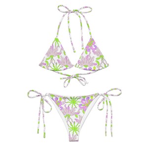 May include: White bikini with a floral print featuring pink and green flowers. The top is a triangle style with adjustable straps and the bottom is a cheeky style with ties on the sides.