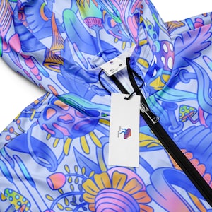 May include: A blue and white lightweight jacket with a psychedelic mushroom print. The jacket has a black zipper and a white tag with the text "Mushroom Kingdom" on it.
